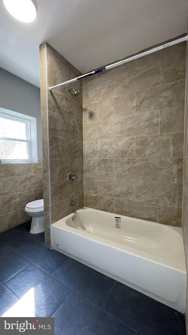 bathroom with tile patterned floors, tiled shower / bath combo, toilet, and tile walls