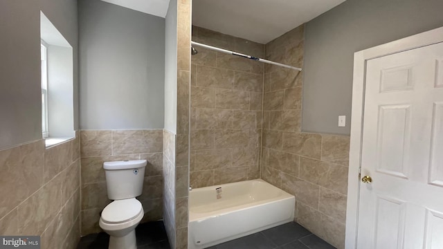 bathroom featuring tile patterned flooring, toilet, tile walls, and tiled shower / bath