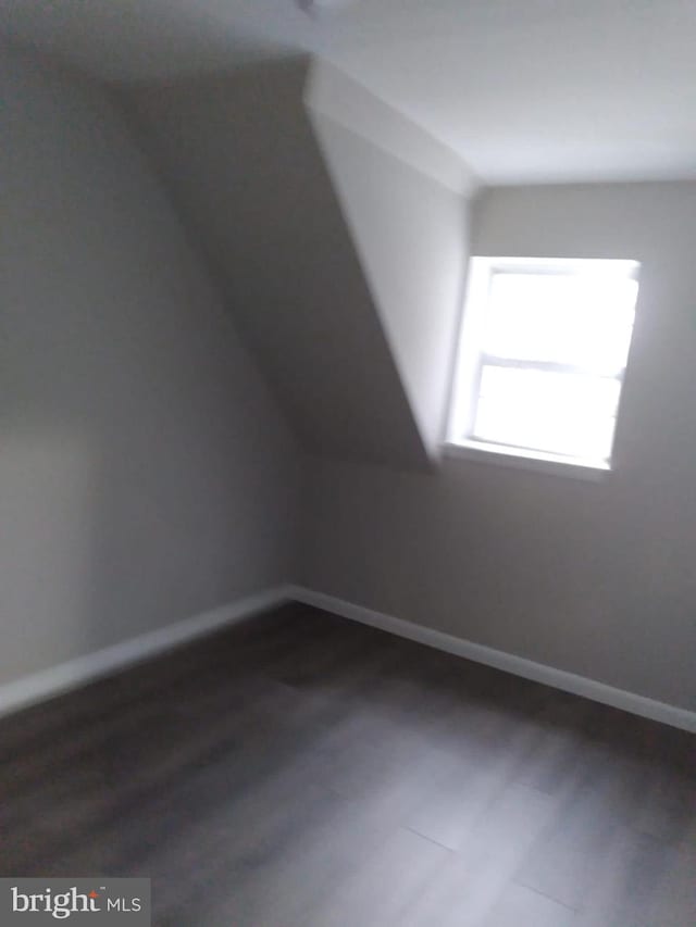 bonus room with dark wood finished floors, lofted ceiling, and baseboards