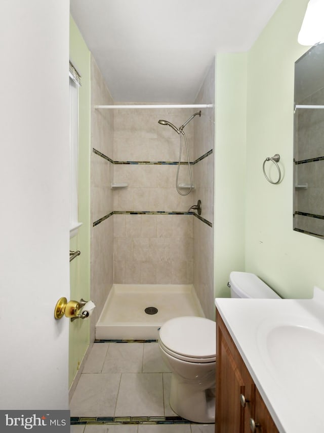 bathroom featuring toilet, vanity, tile patterned flooring, and a tile shower