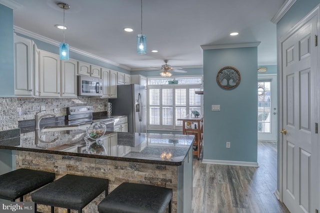 kitchen with kitchen peninsula, backsplash, a breakfast bar, stainless steel appliances, and hardwood / wood-style floors