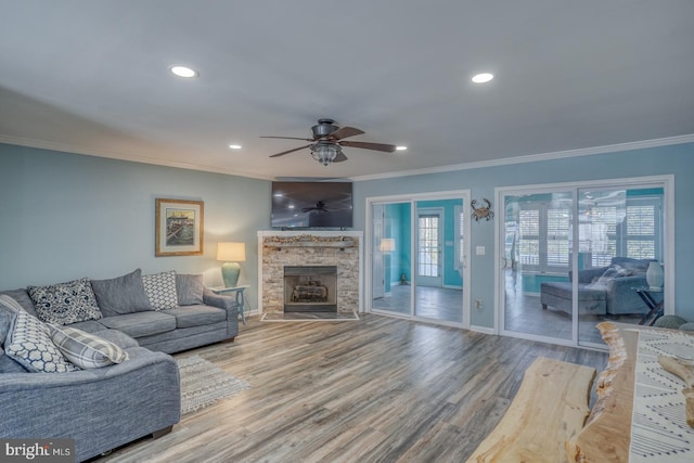 living room with hardwood / wood-style flooring, a stone fireplace, ceiling fan, and ornamental molding