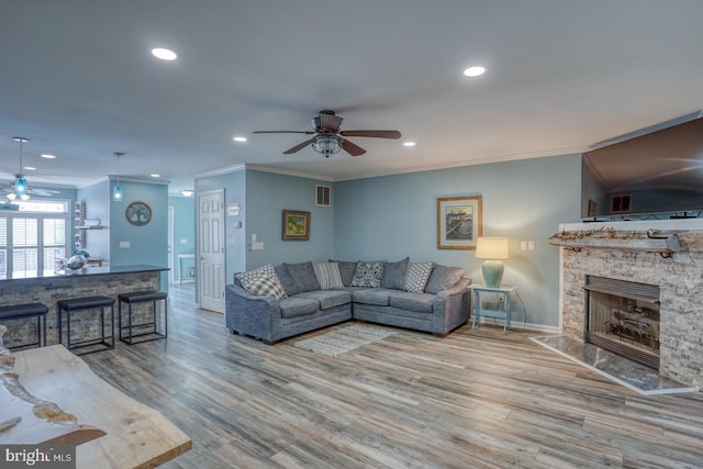 living room with ceiling fan, a stone fireplace, crown molding, and light hardwood / wood-style flooring