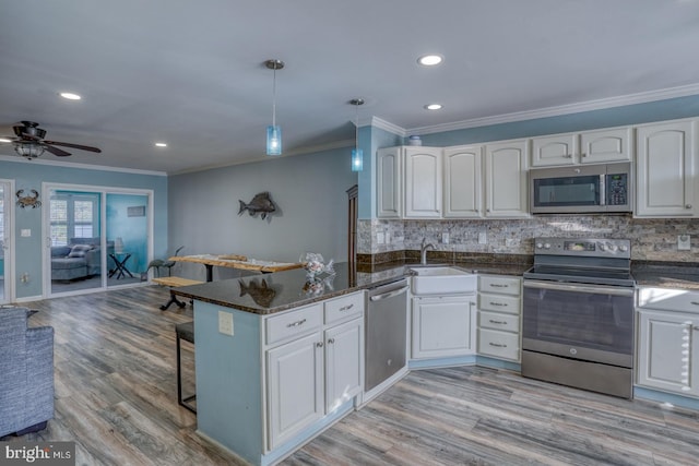 kitchen featuring white cabinets, appliances with stainless steel finishes, kitchen peninsula, and decorative light fixtures