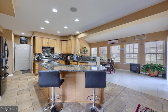 kitchen featuring a breakfast bar, light brown cabinets, dark stone counters, sink, and stainless steel appliances