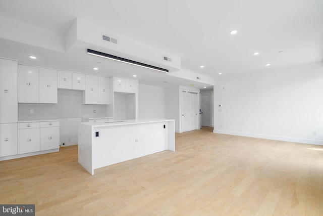 kitchen featuring light hardwood / wood-style floors, decorative backsplash, a center island, and white cabinetry