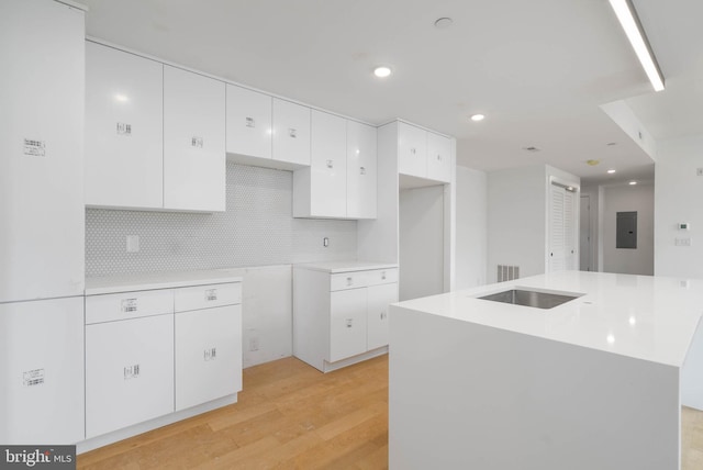 kitchen with tasteful backsplash, electric panel, a center island with sink, white cabinets, and light wood-type flooring