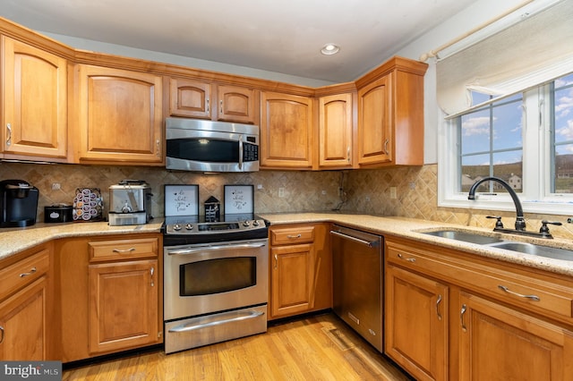 kitchen featuring light stone countertops, sink, stainless steel appliances, tasteful backsplash, and light wood-type flooring