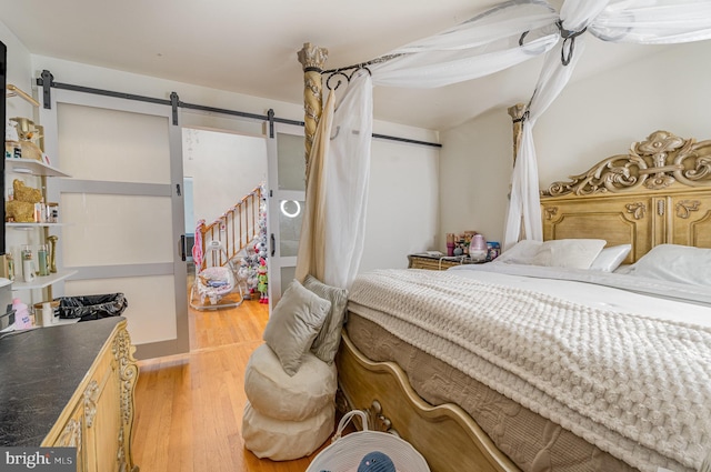 bedroom featuring a barn door, ceiling fan, and light wood-type flooring