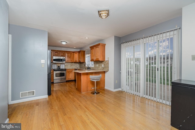 kitchen featuring stainless steel appliances, a kitchen breakfast bar, tasteful backsplash, kitchen peninsula, and light hardwood / wood-style floors