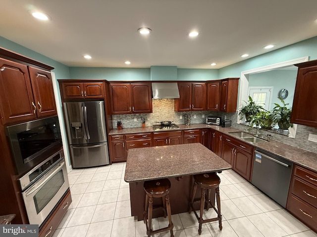 kitchen featuring a center island, wall chimney range hood, sink, a kitchen bar, and stainless steel appliances