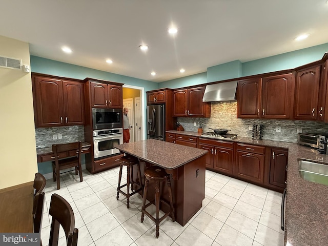 kitchen featuring decorative backsplash, appliances with stainless steel finishes, a kitchen breakfast bar, wall chimney exhaust hood, and a center island