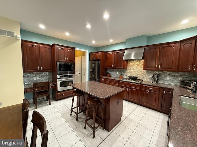 kitchen featuring a breakfast bar, backsplash, stainless steel appliances, and wall chimney range hood