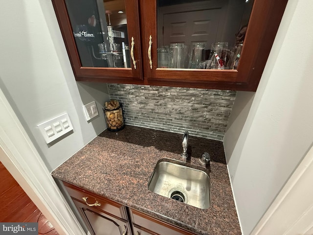 bar featuring backsplash, hardwood / wood-style flooring, dark stone counters, and sink