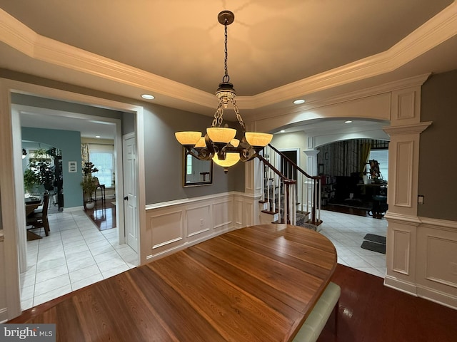 unfurnished dining area featuring an inviting chandelier, crown molding, light hardwood / wood-style flooring, ornate columns, and a tray ceiling