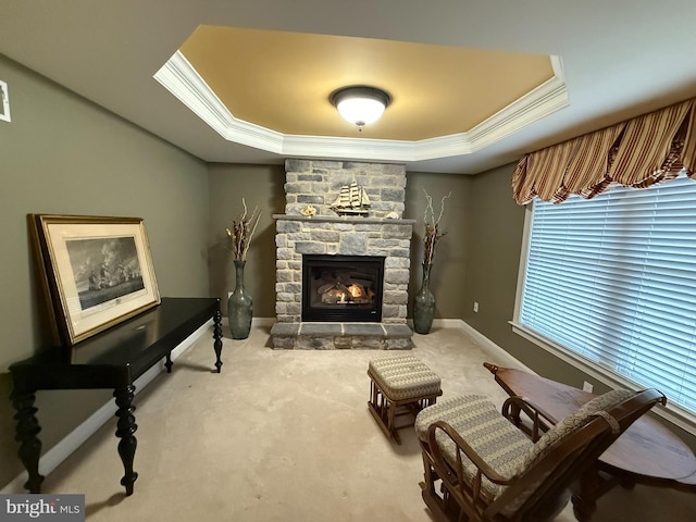 sitting room featuring a tray ceiling, a stone fireplace, crown molding, and carpet