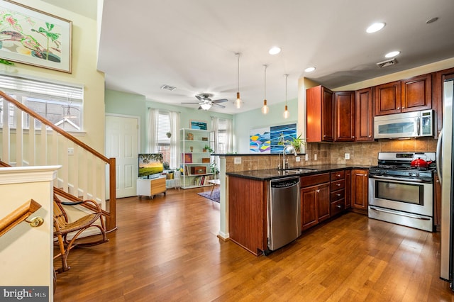 kitchen featuring kitchen peninsula, appliances with stainless steel finishes, ceiling fan, decorative light fixtures, and dark stone countertops