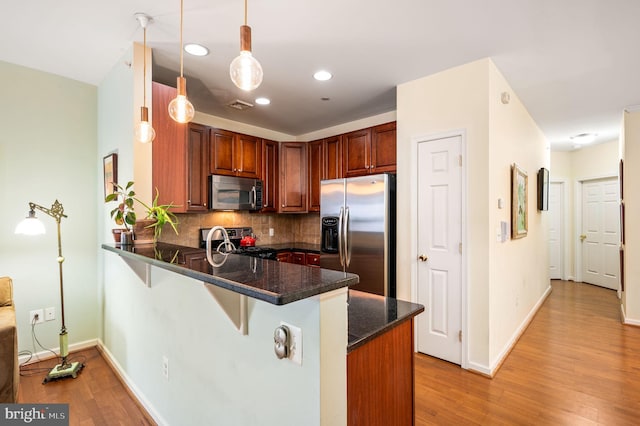 kitchen with kitchen peninsula, a kitchen bar, tasteful backsplash, stainless steel appliances, and hanging light fixtures