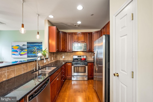 kitchen with sink, hanging light fixtures, stainless steel appliances, light hardwood / wood-style floors, and decorative backsplash