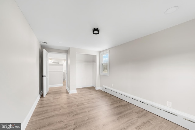 unfurnished bedroom featuring light wood-type flooring and a baseboard heating unit