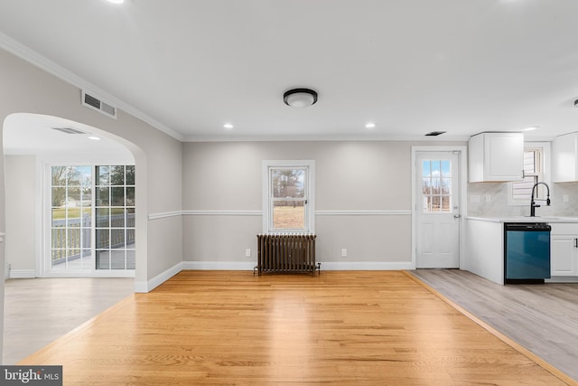 unfurnished dining area with radiator, sink, ornamental molding, and light wood-type flooring