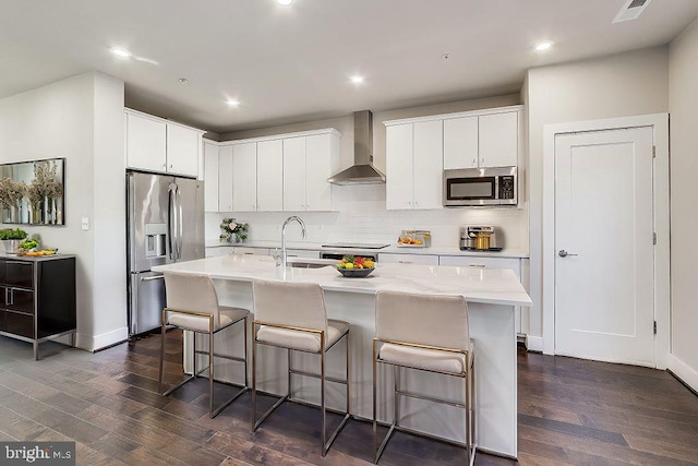 kitchen featuring white cabinetry, wall chimney exhaust hood, dark hardwood / wood-style floors, a center island with sink, and appliances with stainless steel finishes