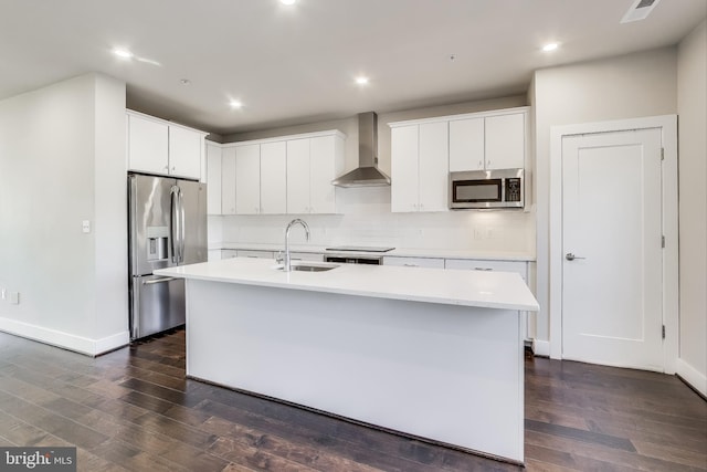 kitchen with wall chimney exhaust hood, stainless steel appliances, sink, a center island with sink, and white cabinets