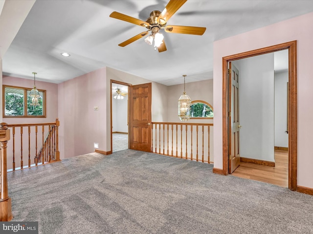 carpeted spare room featuring ceiling fan with notable chandelier