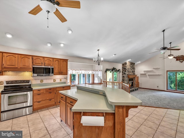 kitchen with a center island, a stone fireplace, vaulted ceiling, light tile patterned floors, and stainless steel appliances