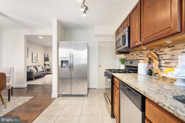 kitchen featuring decorative backsplash, light tile patterned flooring, light stone counters, and stainless steel appliances