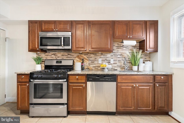 kitchen with backsplash, sink, light stone countertops, light tile patterned floors, and stainless steel appliances