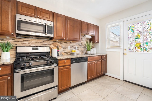 kitchen featuring light stone countertops, appliances with stainless steel finishes, backsplash, and light tile patterned floors