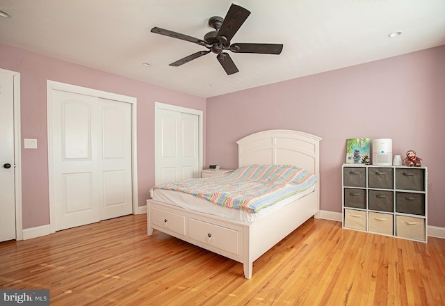 bedroom with light wood-style floors, a ceiling fan, baseboards, and two closets