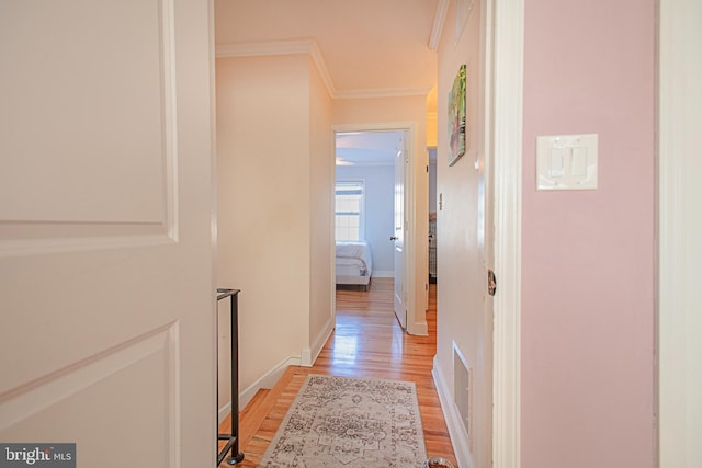 corridor featuring baseboards, ornamental molding, and light wood-style floors