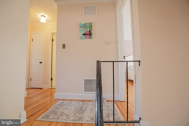 hall featuring baseboards, visible vents, ornamental molding, wood finished floors, and an upstairs landing