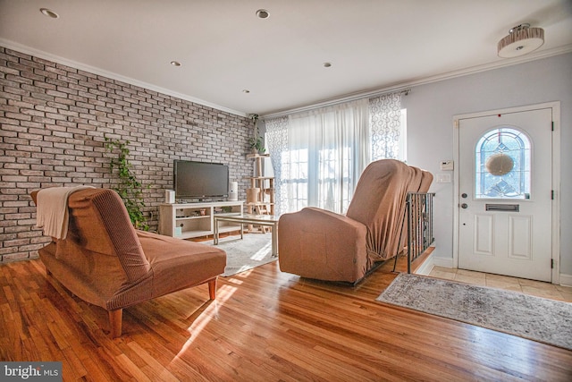 interior space featuring brick wall, baseboards, crown molding, and light wood finished floors