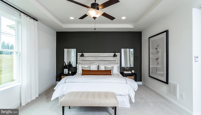 carpeted bedroom with ceiling fan, a raised ceiling, and multiple windows