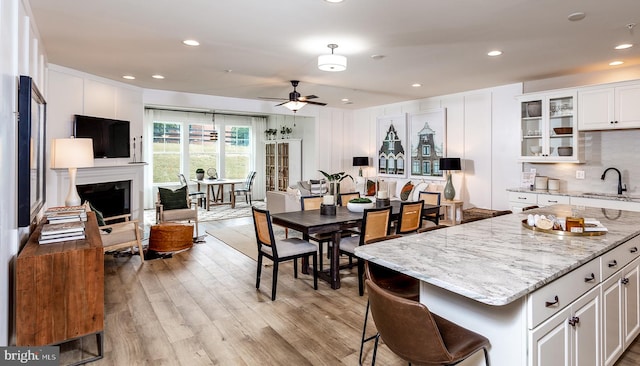 kitchen with light wood-type flooring, white cabinetry, ceiling fan, and light stone counters