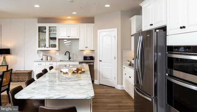 kitchen with light stone countertops, white cabinetry, sink, stainless steel appliances, and a breakfast bar