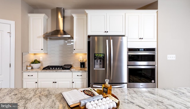 kitchen with white cabinets, light stone counters, wall chimney range hood, and stainless steel appliances