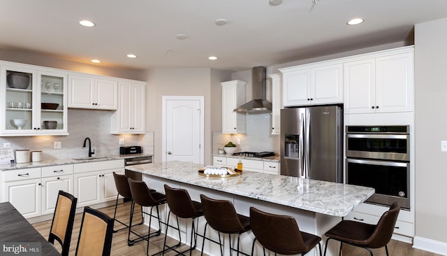 kitchen with white cabinets, stainless steel appliances, wall chimney range hood, and a kitchen island