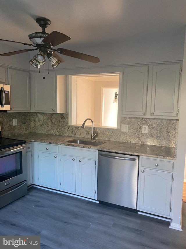 kitchen featuring appliances with stainless steel finishes, light stone counters, dark wood-type flooring, sink, and white cabinets