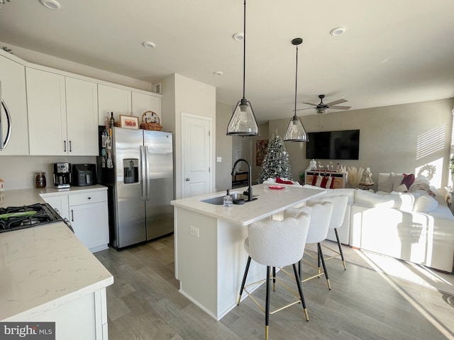 kitchen with ceiling fan, sink, stainless steel fridge with ice dispenser, an island with sink, and pendant lighting