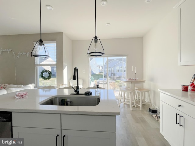 kitchen with pendant lighting, white cabinets, a center island with sink, sink, and light hardwood / wood-style floors