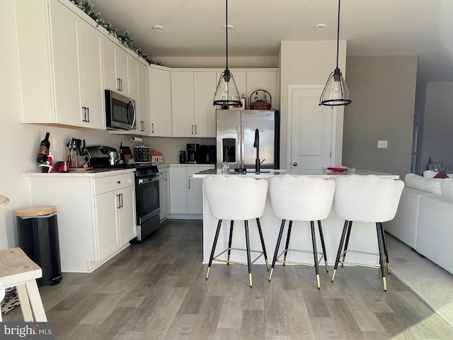 kitchen featuring white cabinetry, a center island, decorative light fixtures, a kitchen bar, and appliances with stainless steel finishes