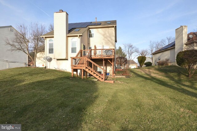 rear view of property featuring a wooden deck, a yard, and solar panels