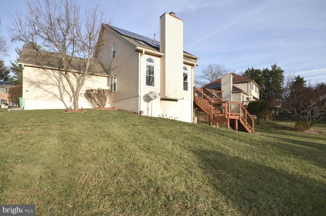 rear view of property with solar panels, a yard, and a wooden deck