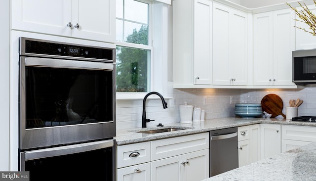 kitchen featuring white cabinetry, sink, light stone countertops, stainless steel appliances, and backsplash