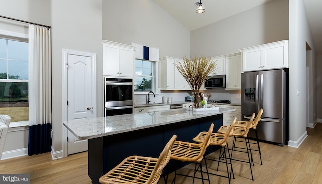 kitchen with light stone countertops, stainless steel appliances, high vaulted ceiling, white cabinets, and a center island