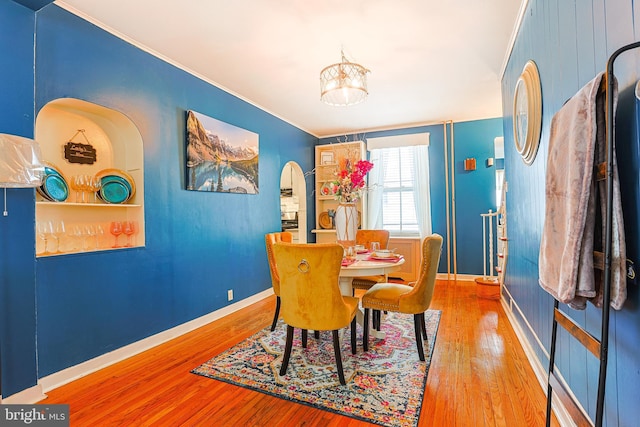 dining space with wood-type flooring, ornamental molding, and a chandelier